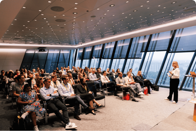 Speaker presenting in a modern conference room with an audience attentively listening, showcasing business insights and strategies.